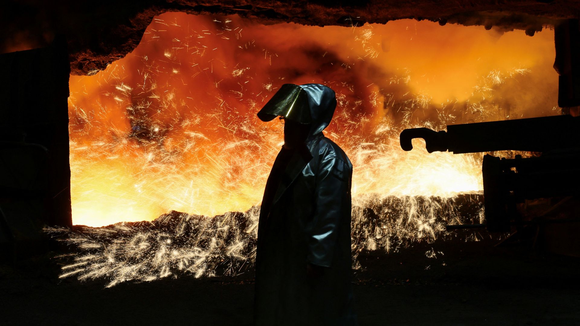 A steel worker in heat protection gear is silhouetted against the sparkling fire of Europe's largest furnace with its daily raw iron production of 12,000 tons, at the steel plant of ThyssenKrupp in Duisburg, Germany. /Wolfgang Rattay/Reuters archive


